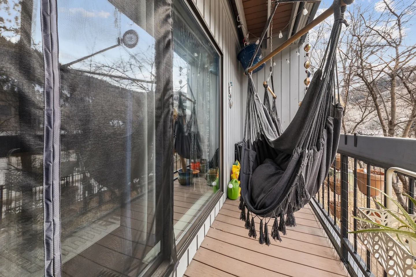 A narrow balcony with plank flooring, a dark hanging hammock chair, and large glass windows and doors.