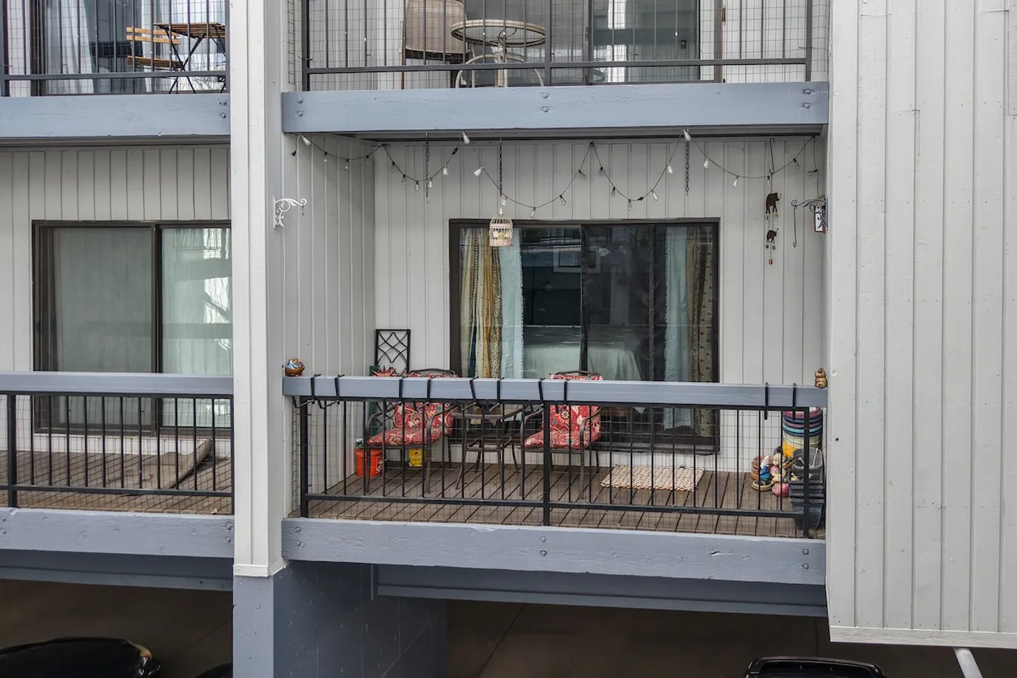 Exterior view of an apartment or condo balcony featuring outdoor chairs, decorative string lights, and a sliding glass door.
