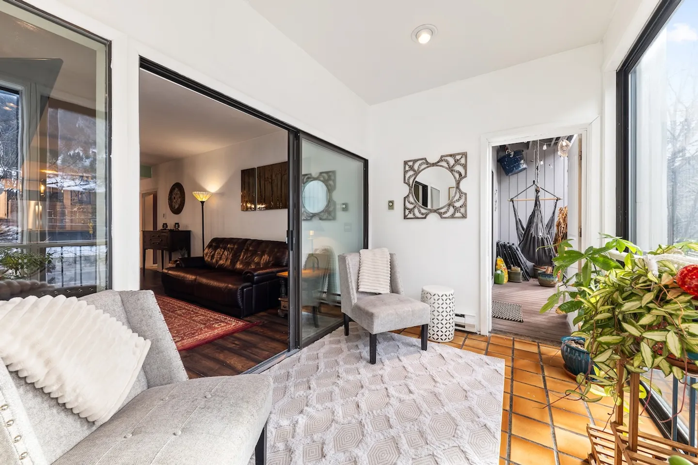 Sunroom with tiled floor, armchairs, and a view into the adjoining living room through sliding glass doors.