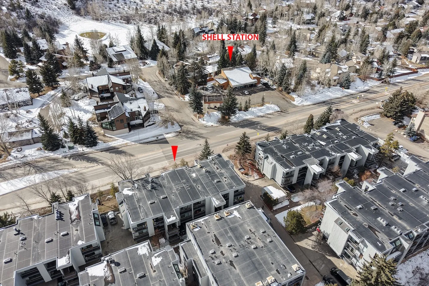 Aerial view of a condominium complex and surrounding neighborhood with snow on the ground, trees, and roads.