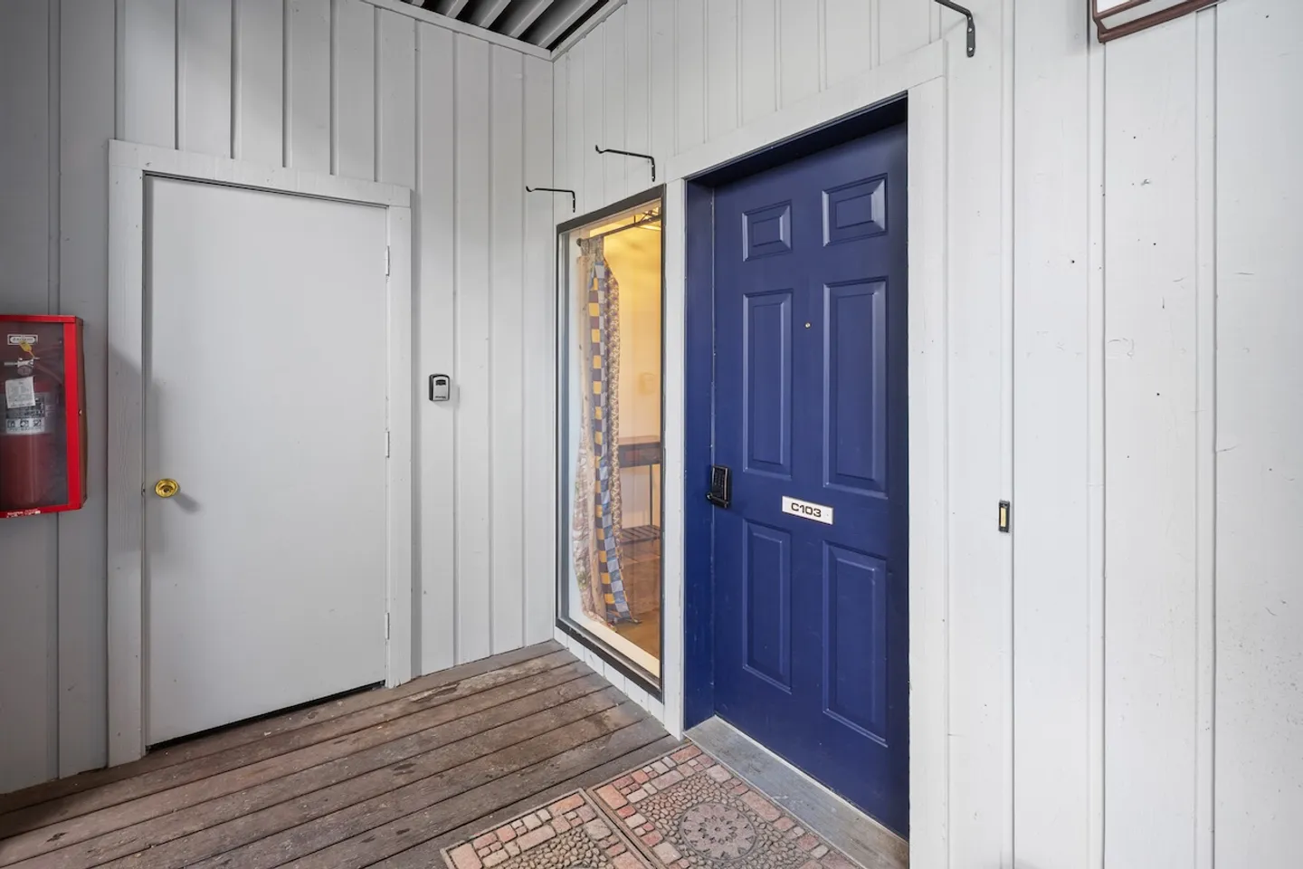 Exterior covered entryway featuring a dark blue front door labeled C103, a small adjacent window, and a white side door.