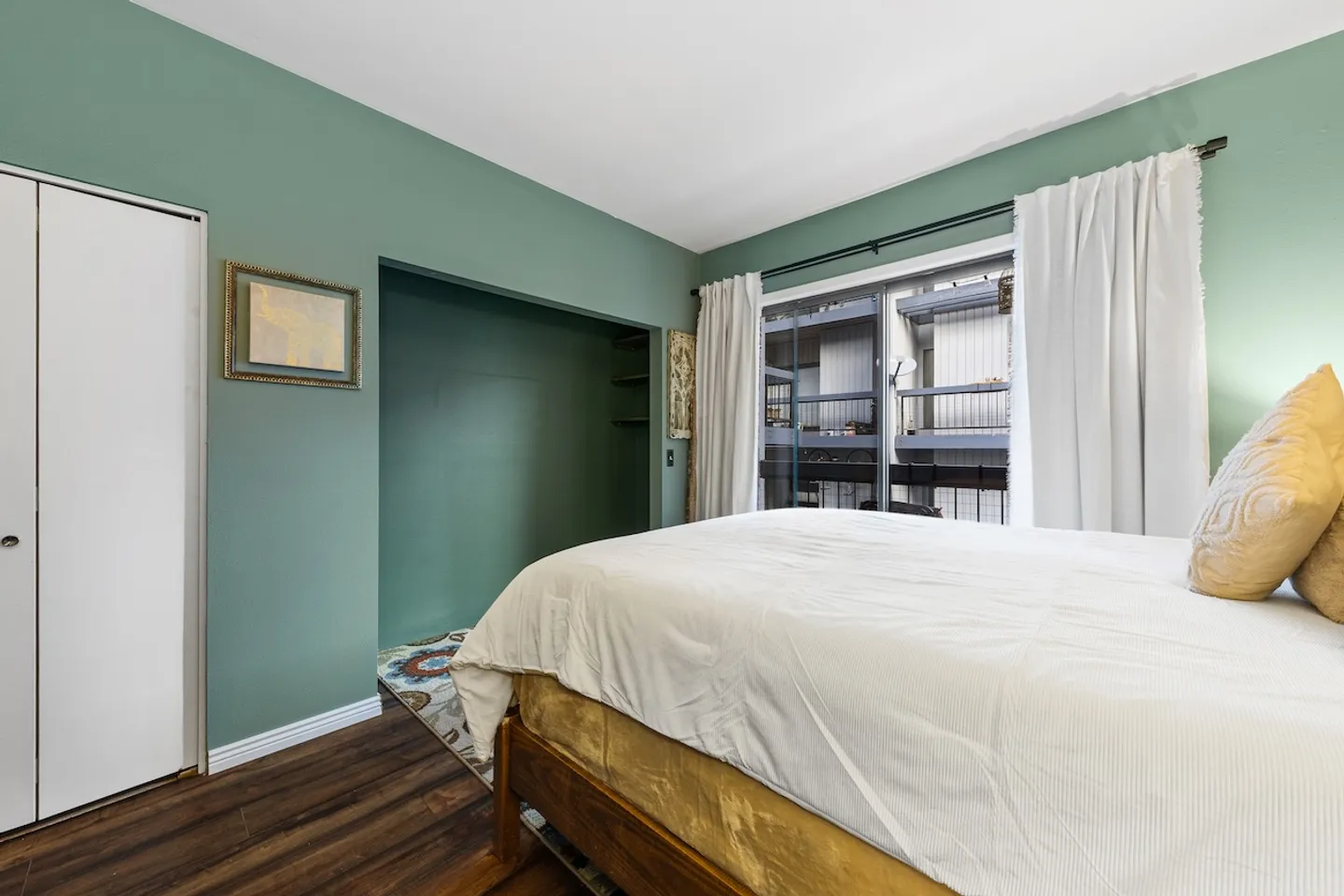 Bedroom with sage green walls, wood flooring, a bed, a recessed closet nook, and sliding glass doors leading outside.