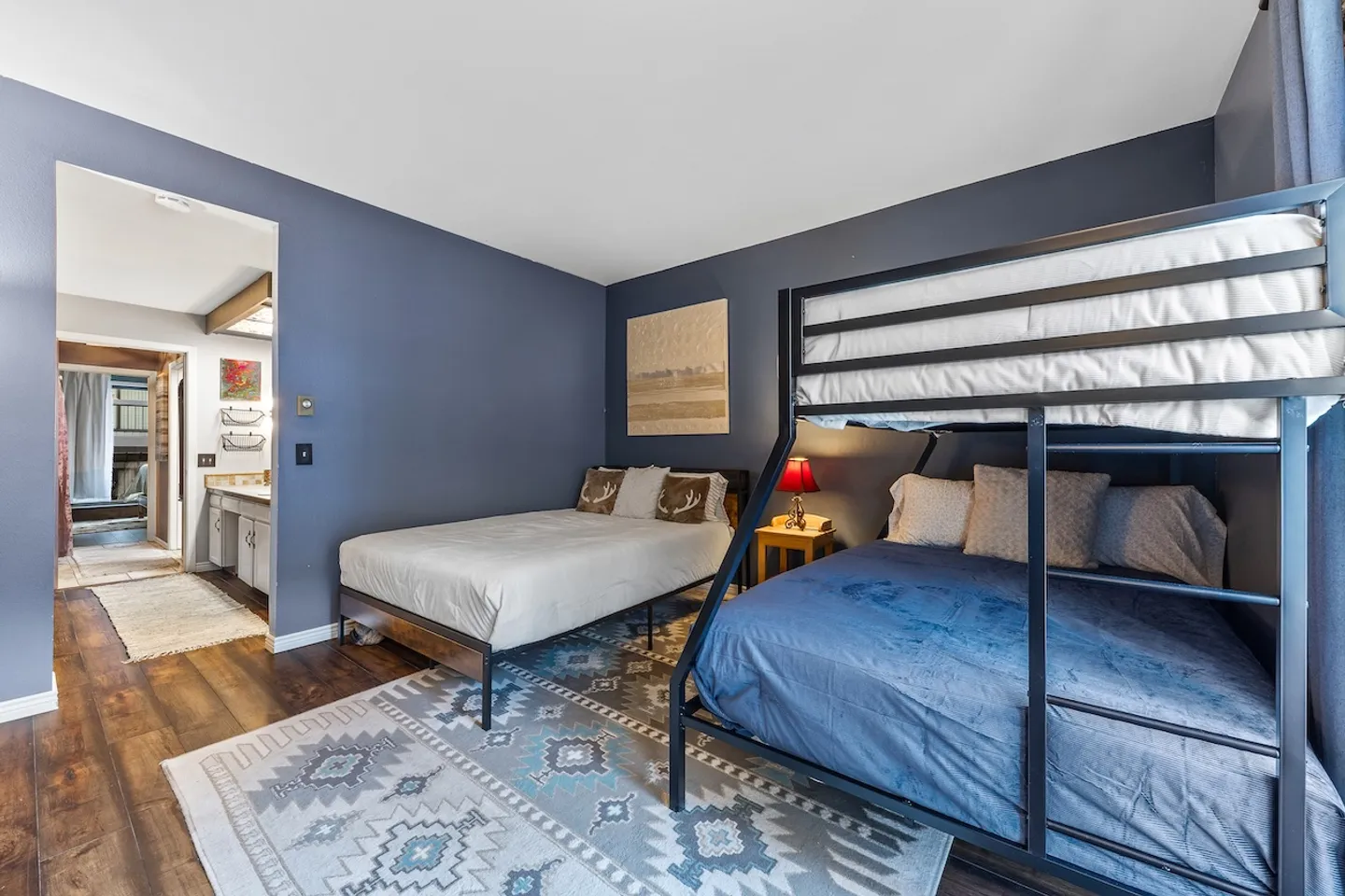 Bedroom featuring dark blue walls, a metal bunk bed, a second bed, and wood-look flooring with an area rug leading toward a bathroom.
