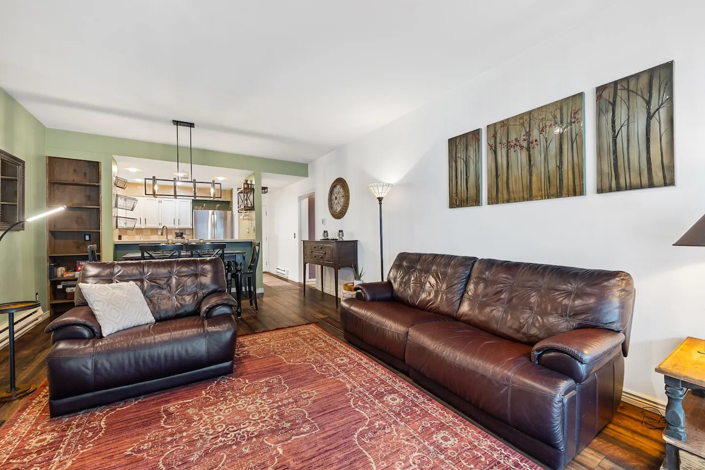 Living room with brown leather seating, an area rug, and a view into the open kitchen.