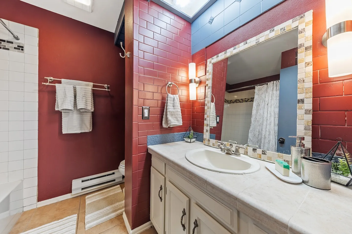 Bathroom with red tiled walls, a tiled vanity counter, framed mirror, and wall sconces.