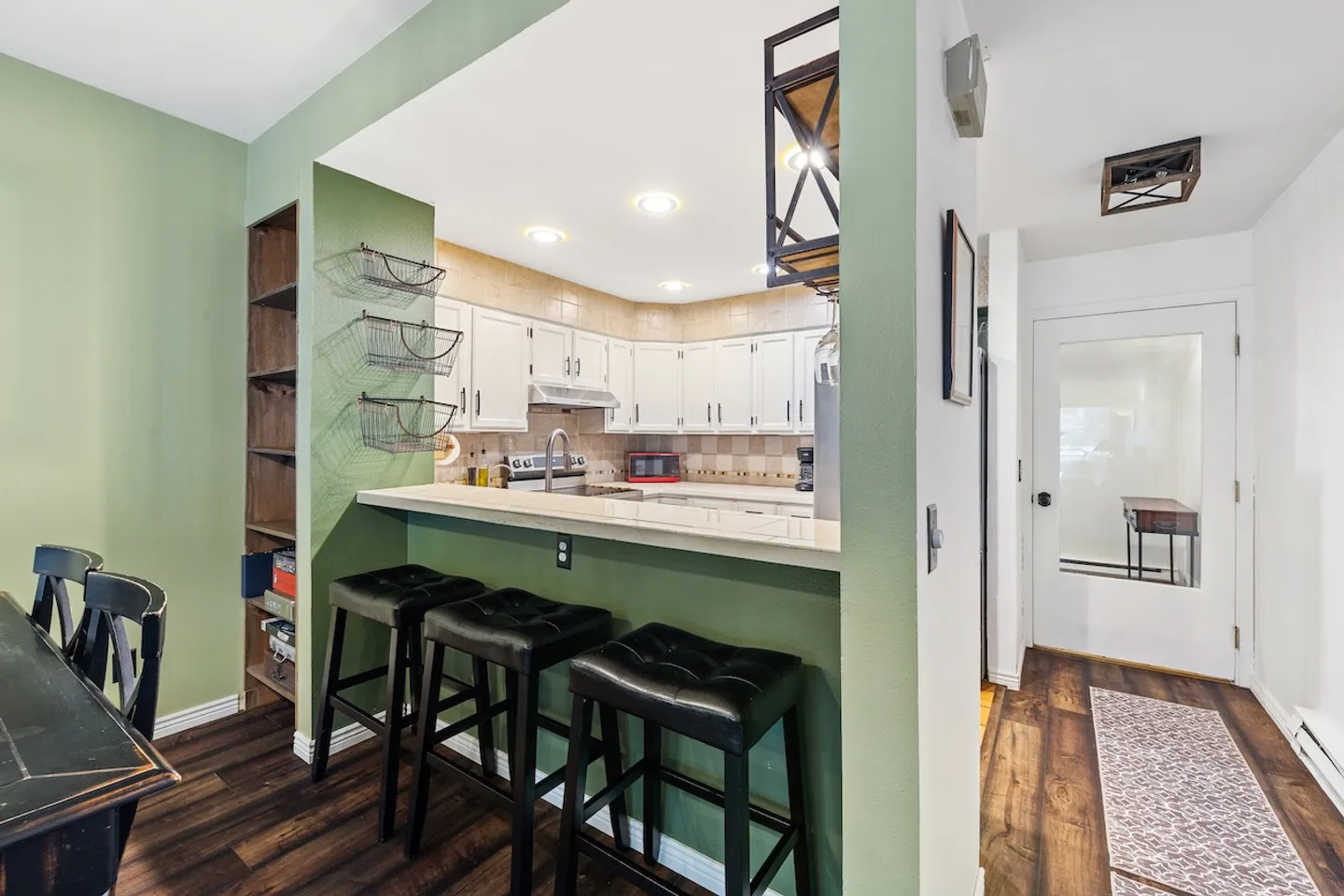 Kitchen pass-through breakfast bar with three black leather-topped barstools and a view into the kitchen with white cabinetry.