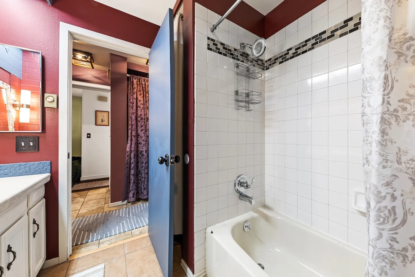 Bathroom showing a tiled bathtub and shower combination with deep red walls and a view into the hallway.
