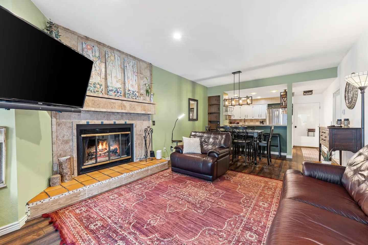 Living room with a tiled fireplace, mounted TV, leather seating, and open view into the dining area and kitchen.