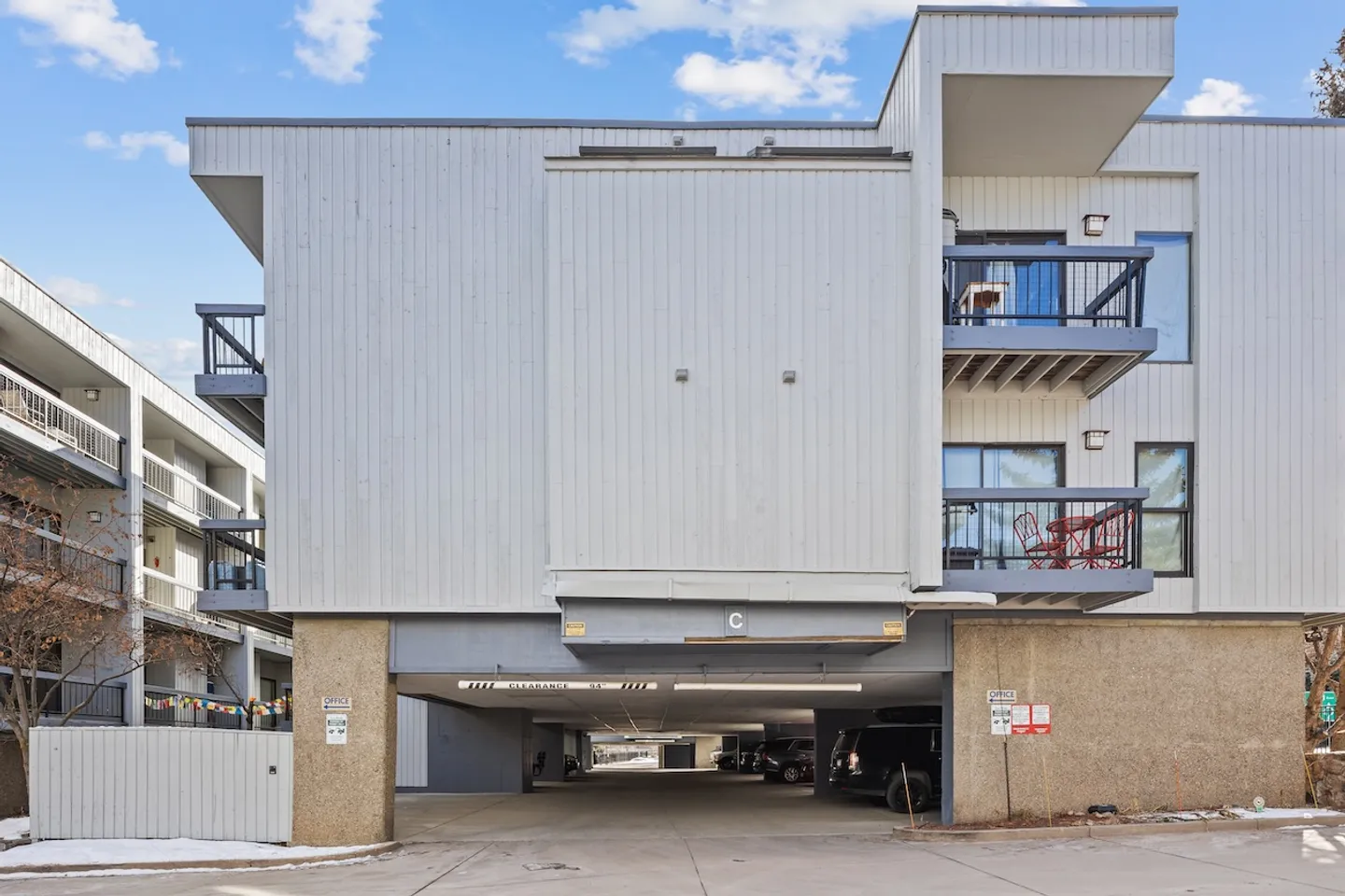 Exterior of a multistory gray building with a covered ground-level parking garage entrance beneath it.