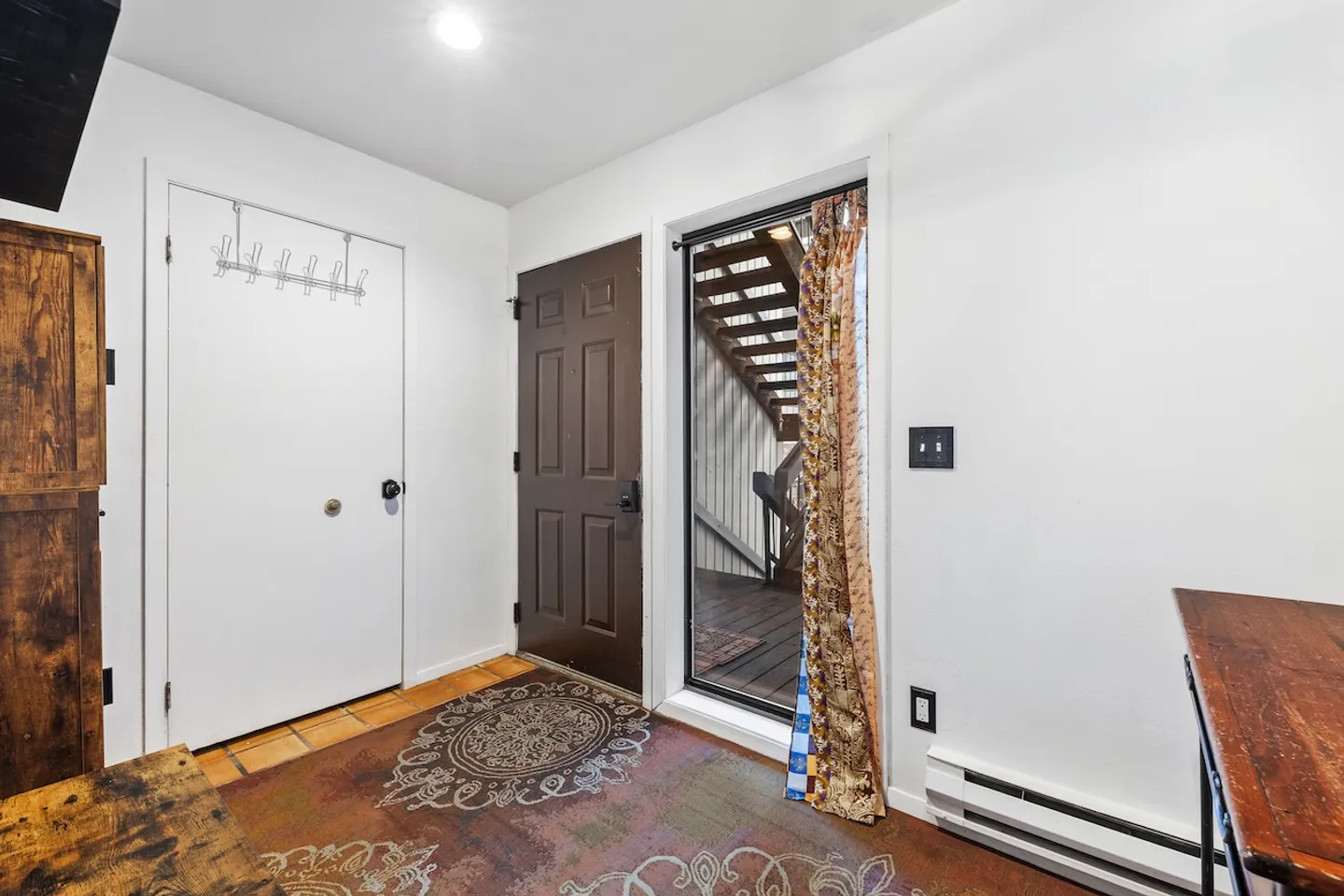 Entryway with a patterned area rug, a dark front door, a white interior door, and an exterior door opening onto a wooden deck with stairs.