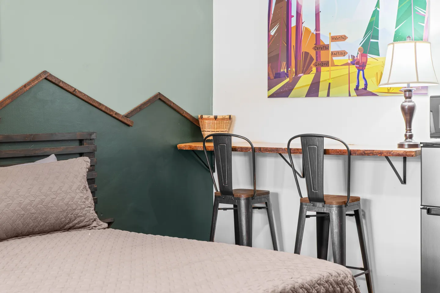 Bedroom featuring a bed with a quilted coverlet beside a wall-mounted wooden counter with two metal barstools.