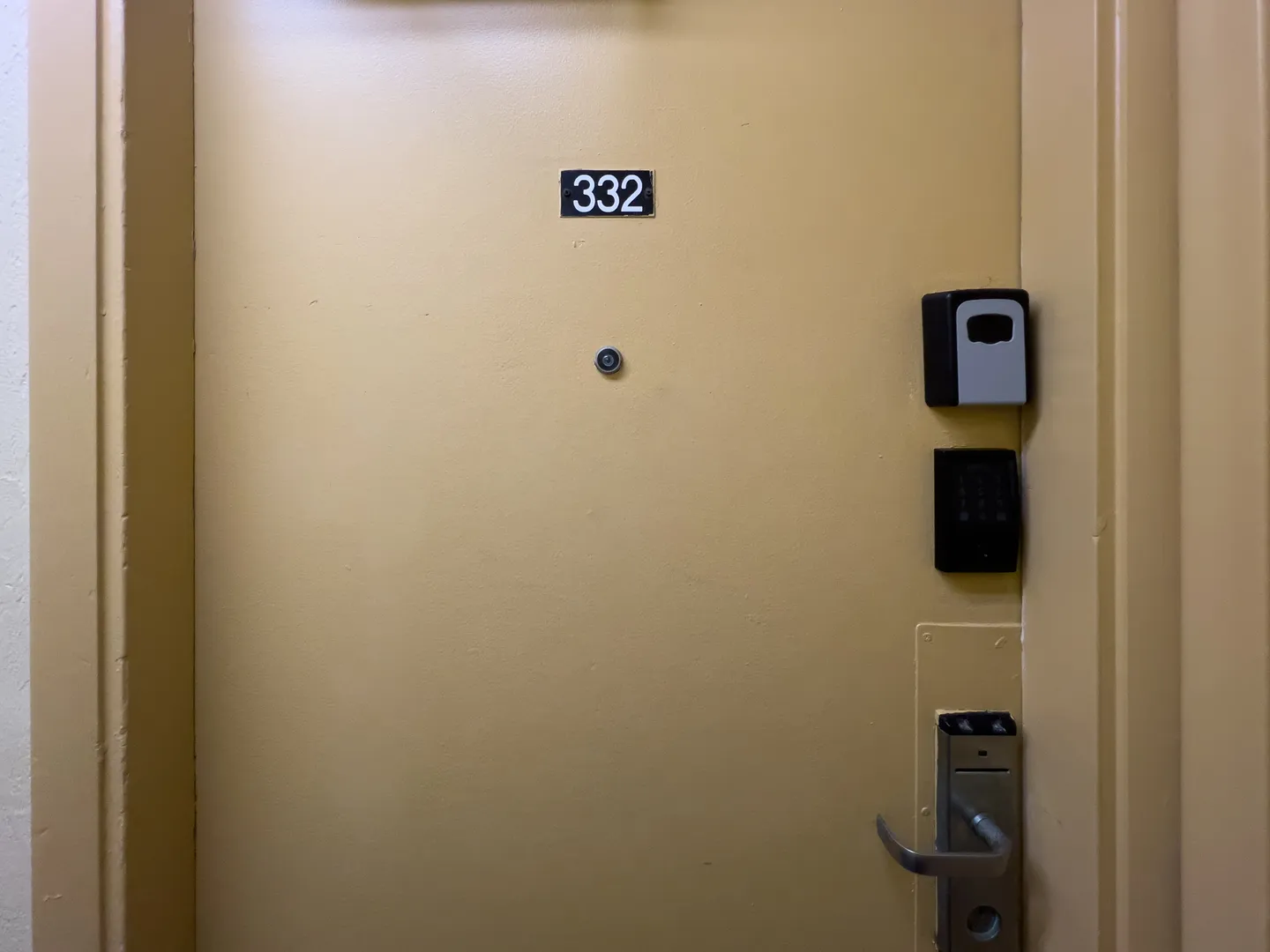 Yellow unit entry door labeled with number 332 featuring electronic locks and a lockbox.
