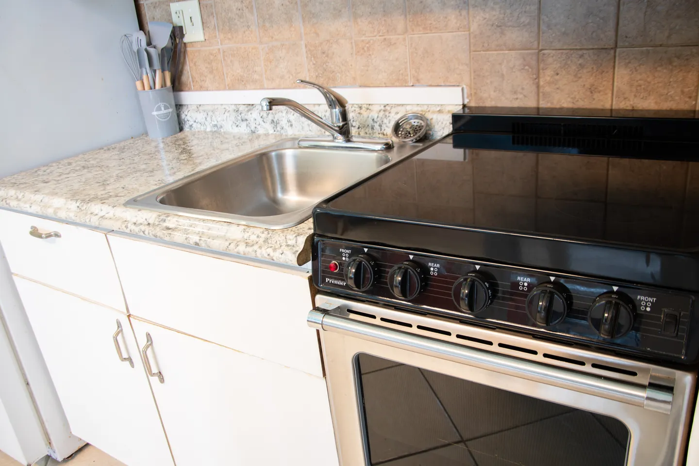 Close-up of a kitchen corner featuring a stainless steel sink, speckled countertop, and a black and stainless steel range.