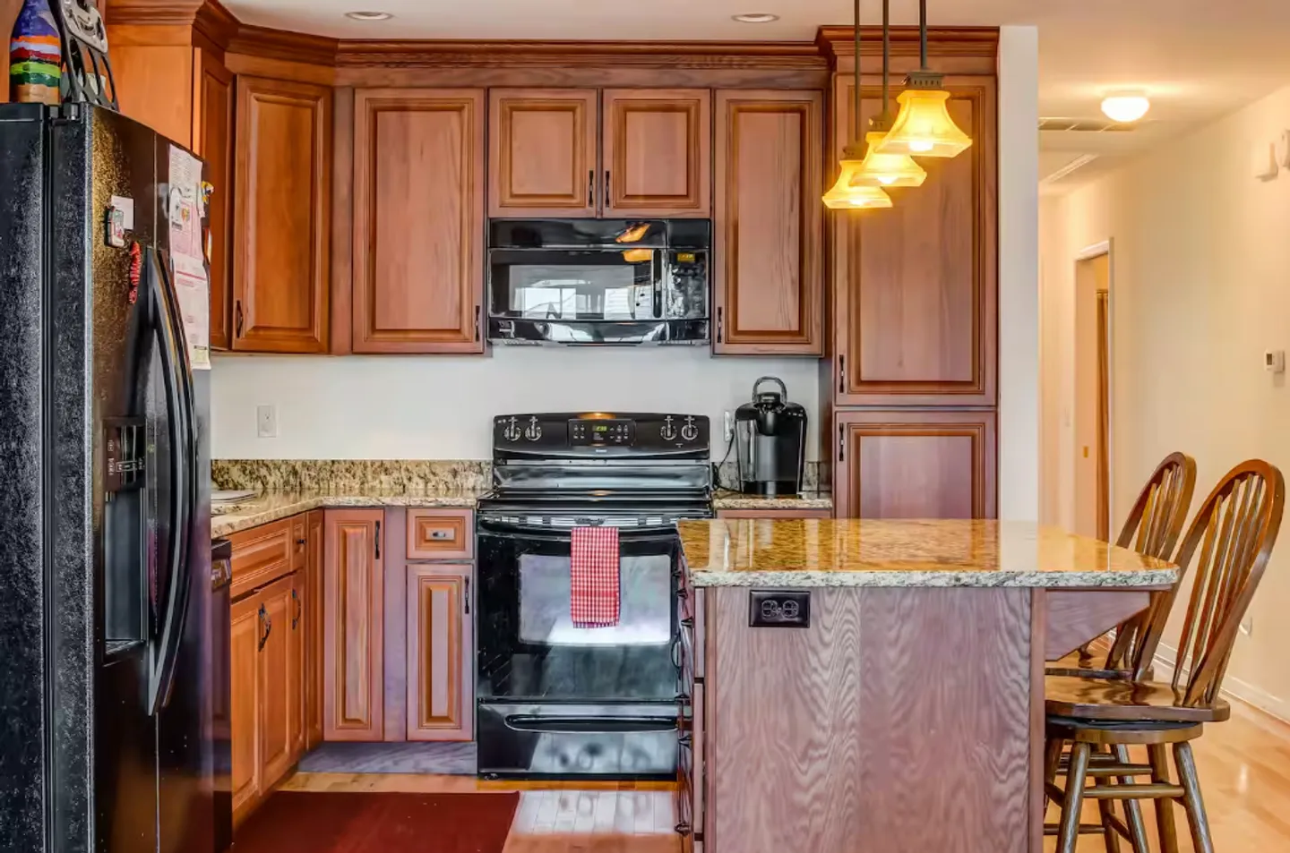 Kitchen with warm wood cabinetry, granite countertops, black appliances, and an island with wooden barstools.