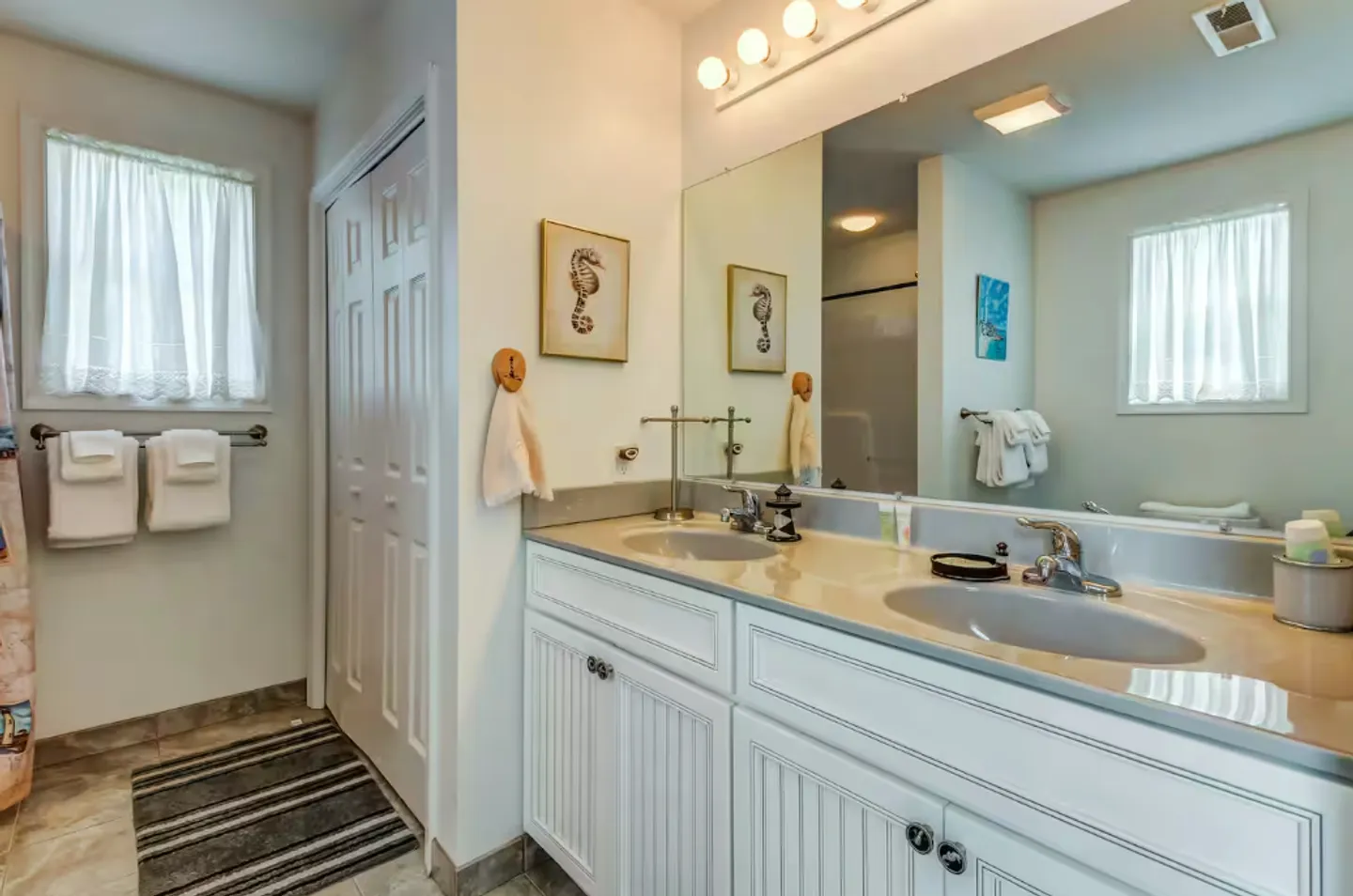 Bathroom with a double-sink vanity, large frameless mirror with globe vanity lights, and white louvered closet doors.