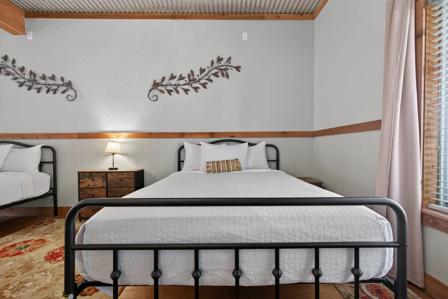 Bedroom featuring black metal frame beds dressed in white bedding, with wood trim and decorative metal wall art.