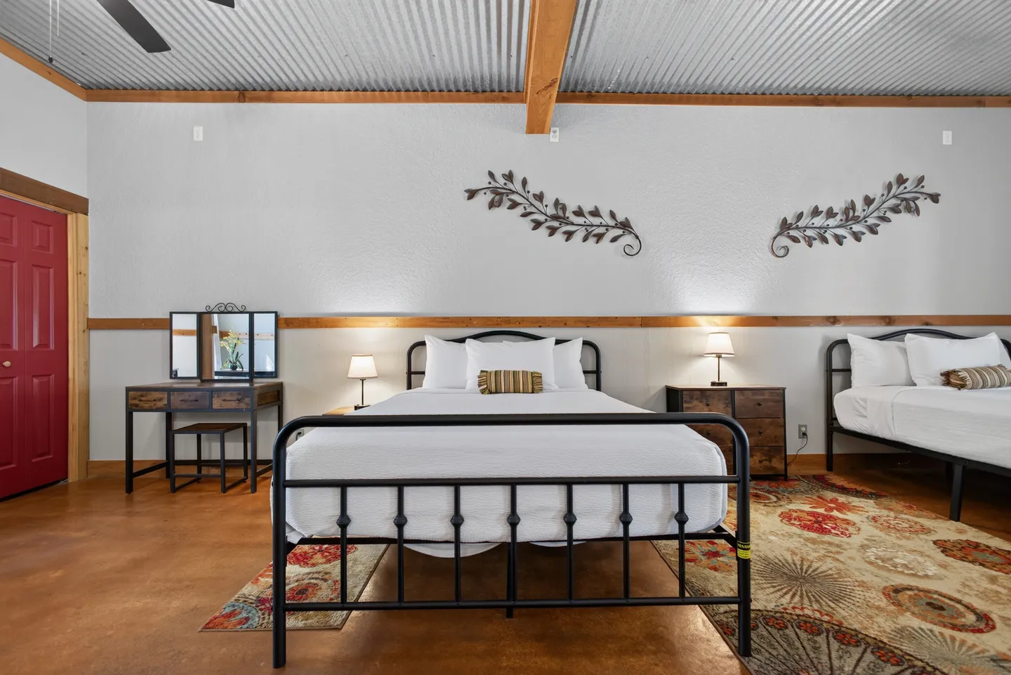 Bedroom with two black metal frame beds, corrugated metal ceiling, and a vanity table.