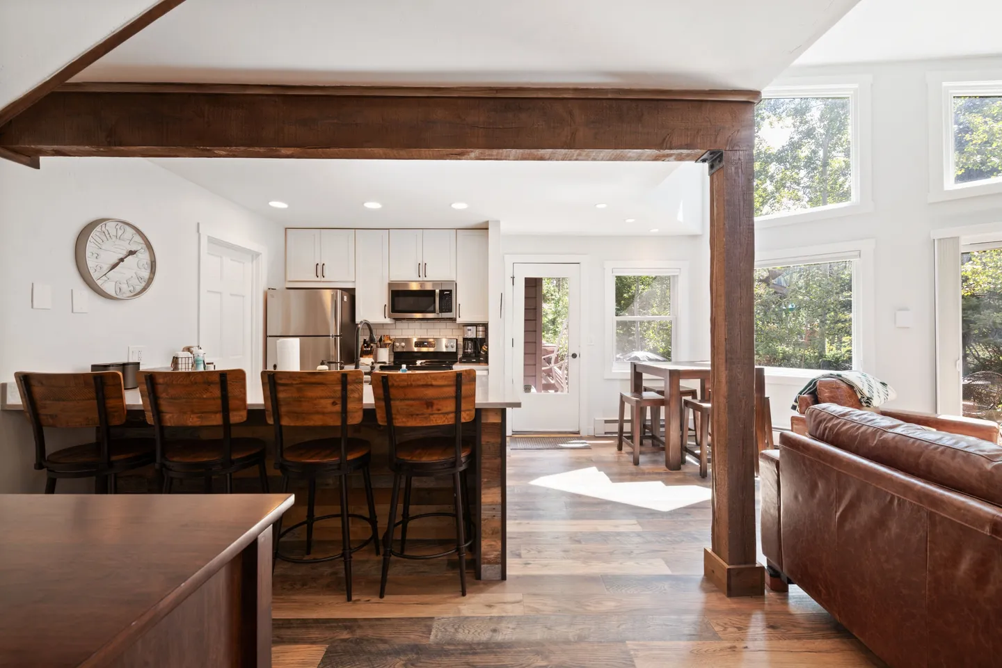 Open concept kitchen and living area framed by an exposed wooden beam with bar seating, white cabinets, and wood-look flooring.