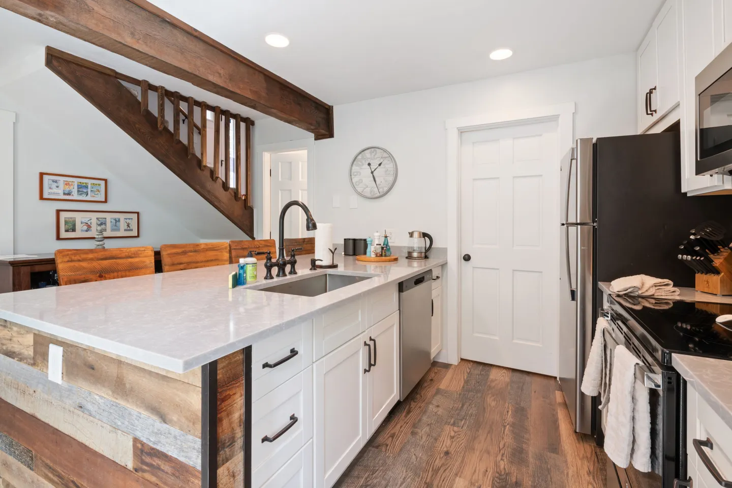 Kitchen island with an undermount sink and black faucet, white shaker cabinets, stainless steel appliances, and wood-paneled accents beneath an exposed ceiling beam.
