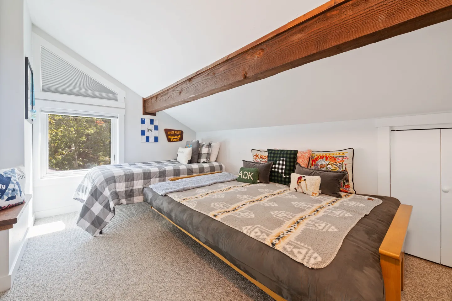 Bedroom with sloped ceiling, exposed wood beam, carpeted floor, a low bed, and a twin bed under a window.