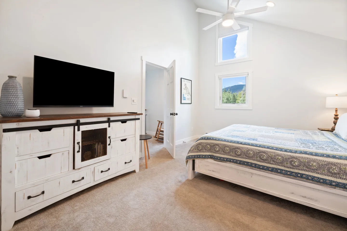 Bedroom featuring vaulted ceilings, a ceiling fan, a mounted TV above a rustic dresser, and a bed with a patterned quilt.