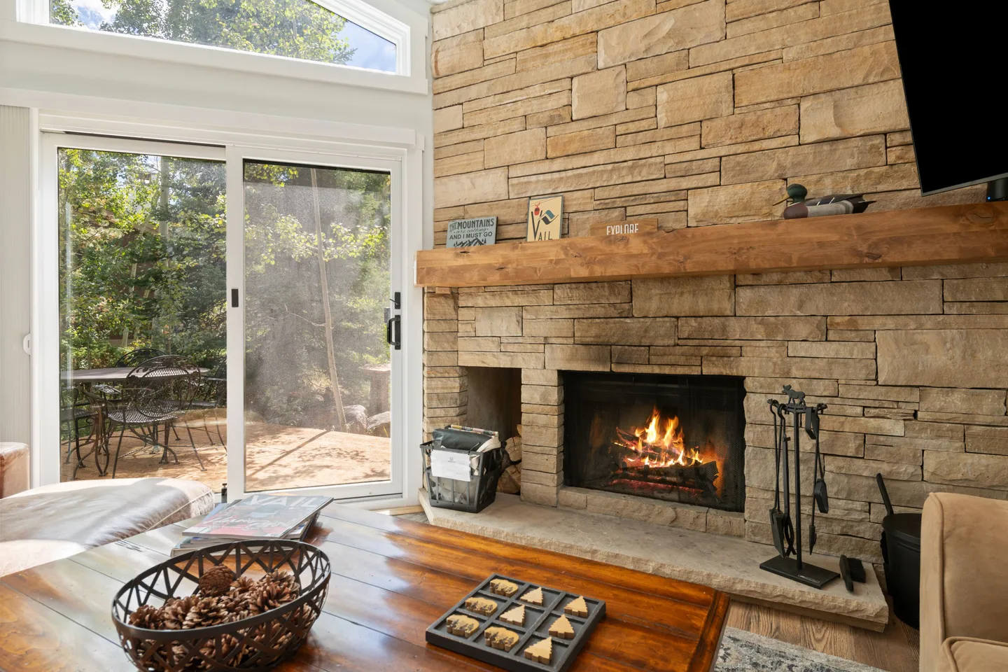 Living room with a stone-clad wood-burning fireplace, a wooden mantel, and sliding glass doors opening to an outdoor patio.