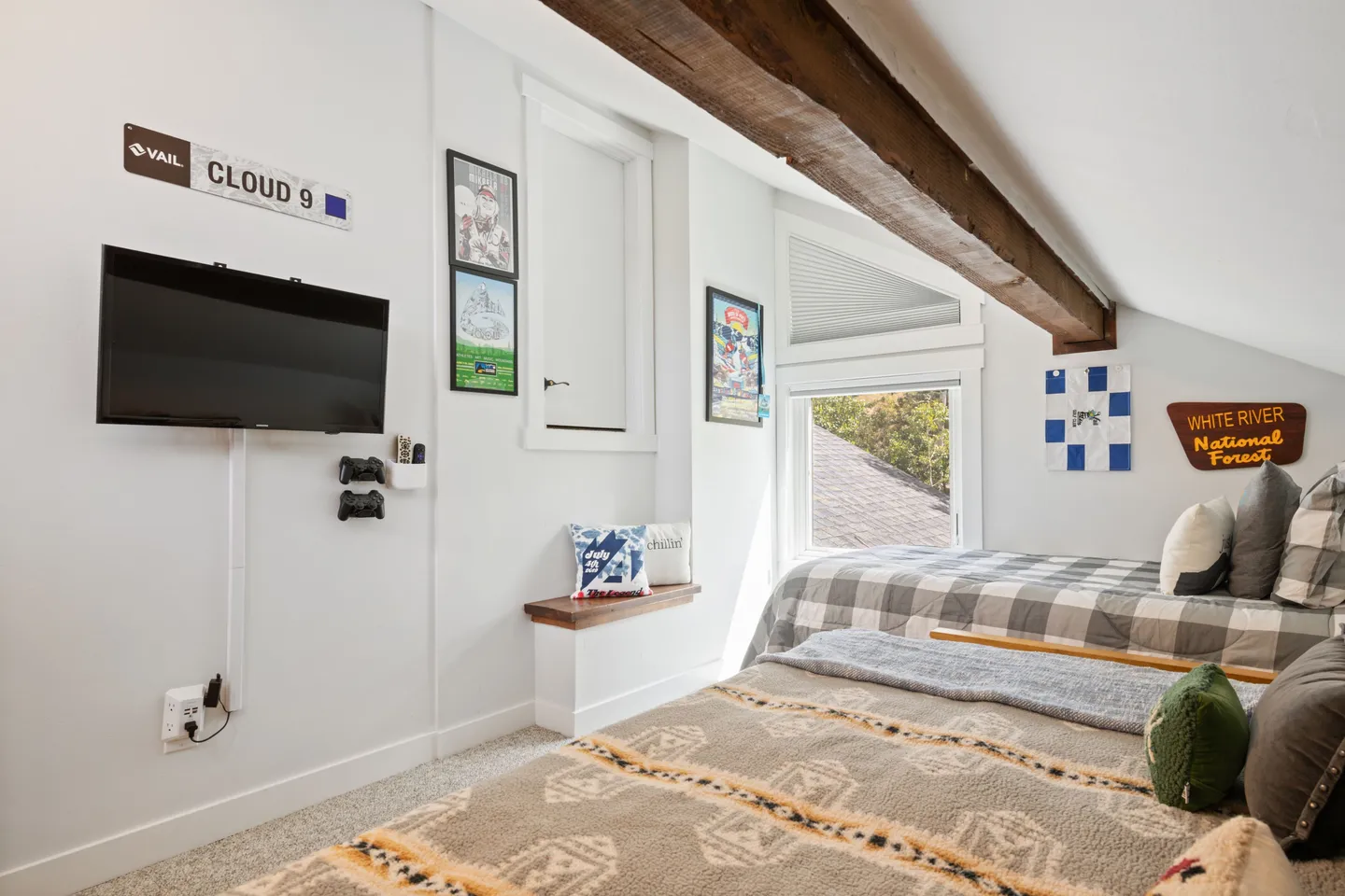Attic bedroom featuring two beds with patterned bedding, a sloped ceiling with an exposed wood beam, and a wall-mounted TV.