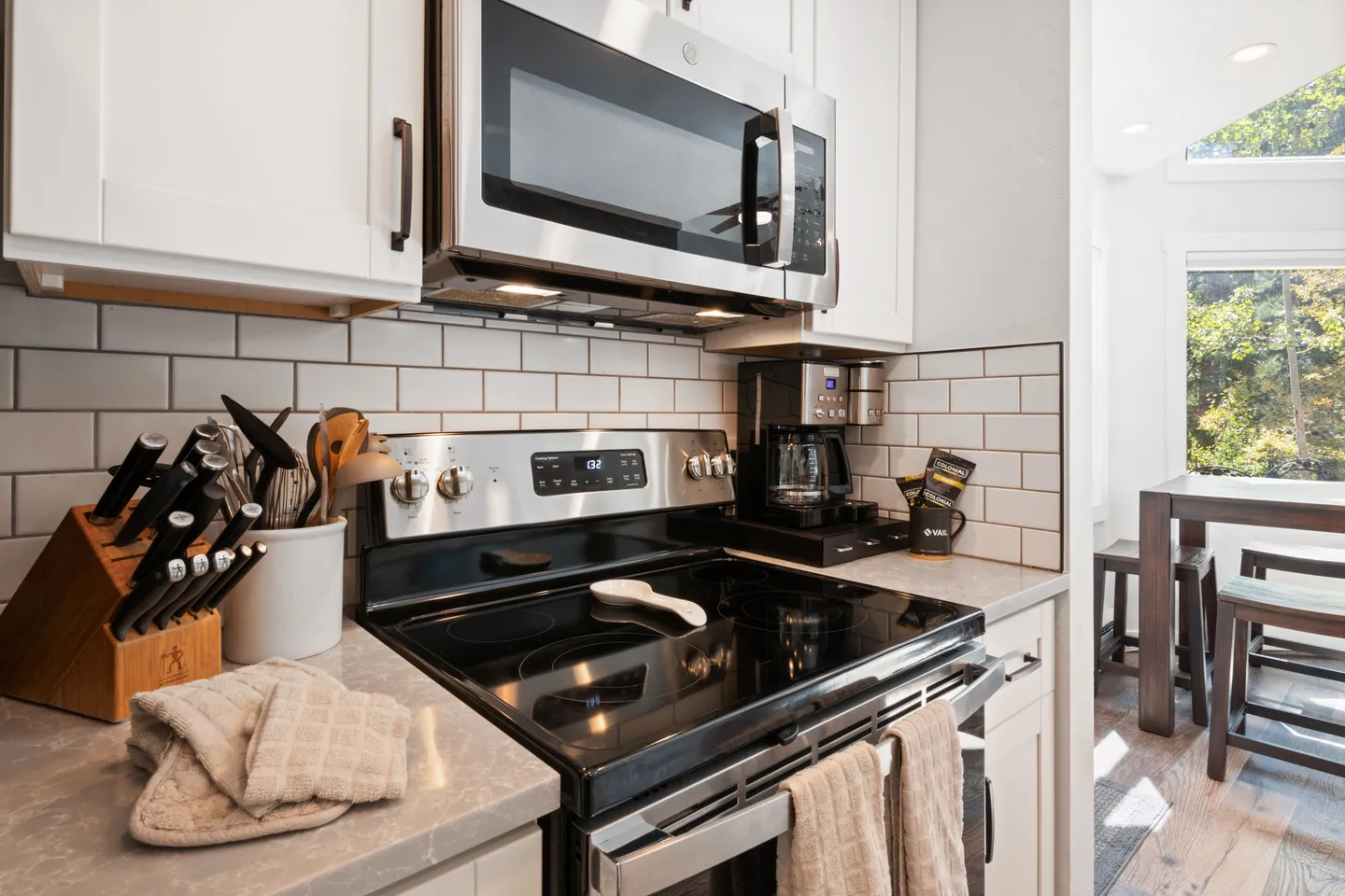 Kitchen counter area with an electric range, over-the-range microwave, knife block, and coffee maker against a white subway tile backsplash.