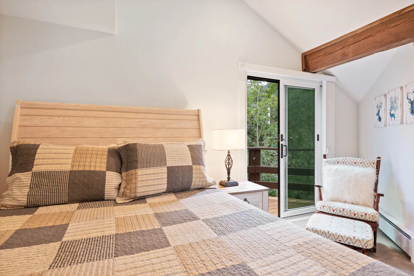 Bedroom featuring a bed with a patchwork quilt, a nightstand with a lamp, a rocking chair with an ottoman, and sliding glass doors leading to a balcony.