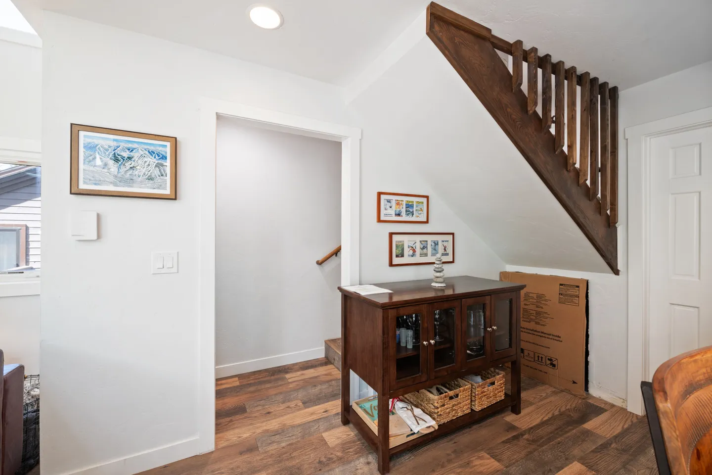 Hallway and under-stair area with wood-look flooring, a wooden sideboard cabinet, and framed wall art.