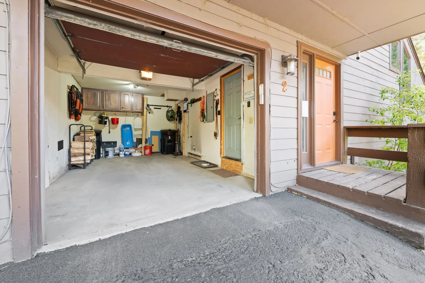 Exterior view showing an open single-car garage with storage and firewood alongside a covered front porch and entry door.