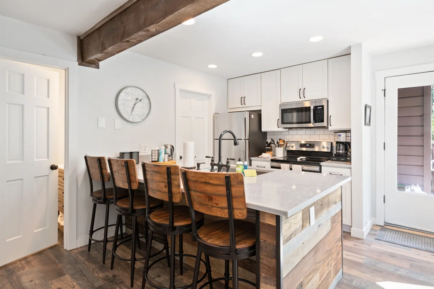 Kitchen with white cabinetry, stainless steel appliances, and an island counter with four wooden barstools.