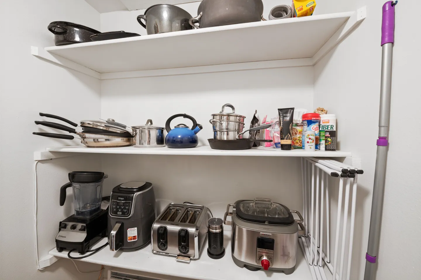 Pantry shelves stocked with kitchen appliances, cookware, pots, pans, a kettle, and a drying rack.
