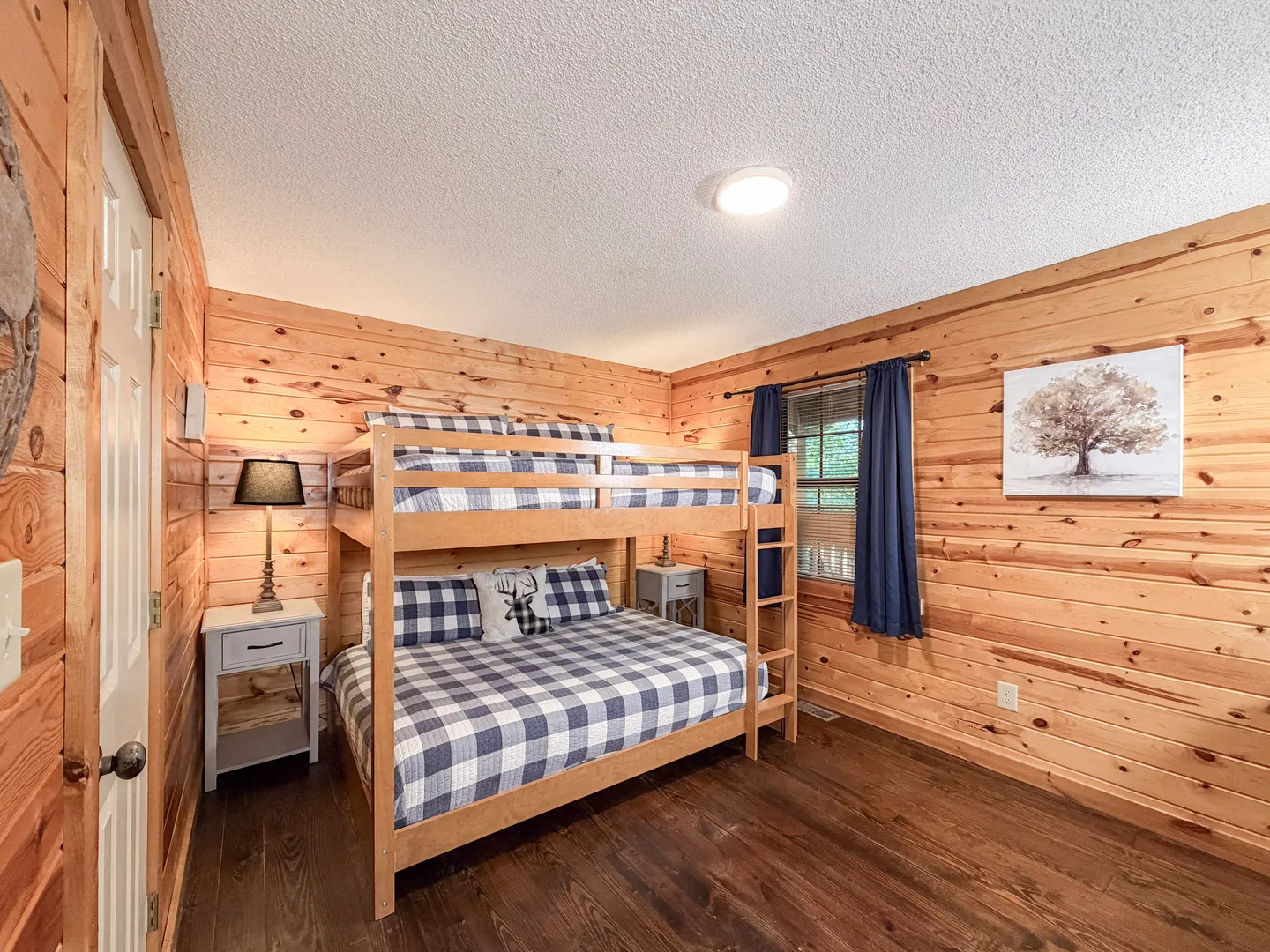 Bedroom with knotty pine wood paneled walls, dark wood flooring, and a wooden bunk bed with blue plaid bedding.