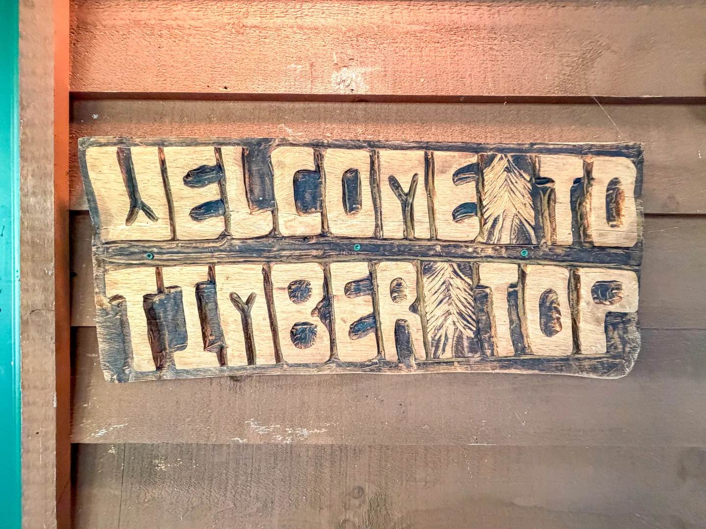 Carved wooden sign reading Welcome to Timber Top mounted on horizontal wood siding.