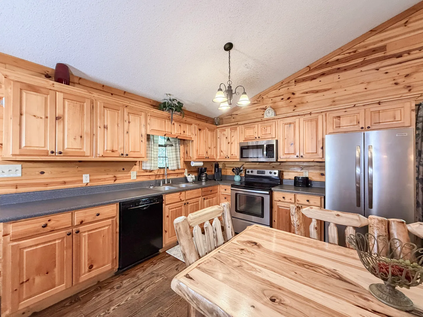 Kitchen with knotty pine cabinetry and walls, stainless steel refrigerator and stove, and a log-style dining table in the foreground.