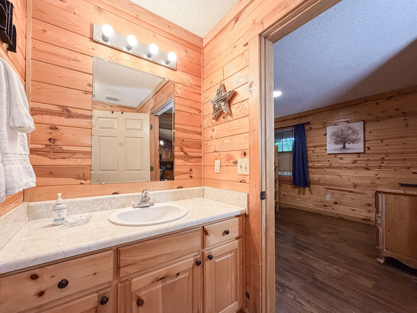 Bathroom vanity with wooden paneled walls and a mirror, looking into an adjoining wood-paneled bedroom.
