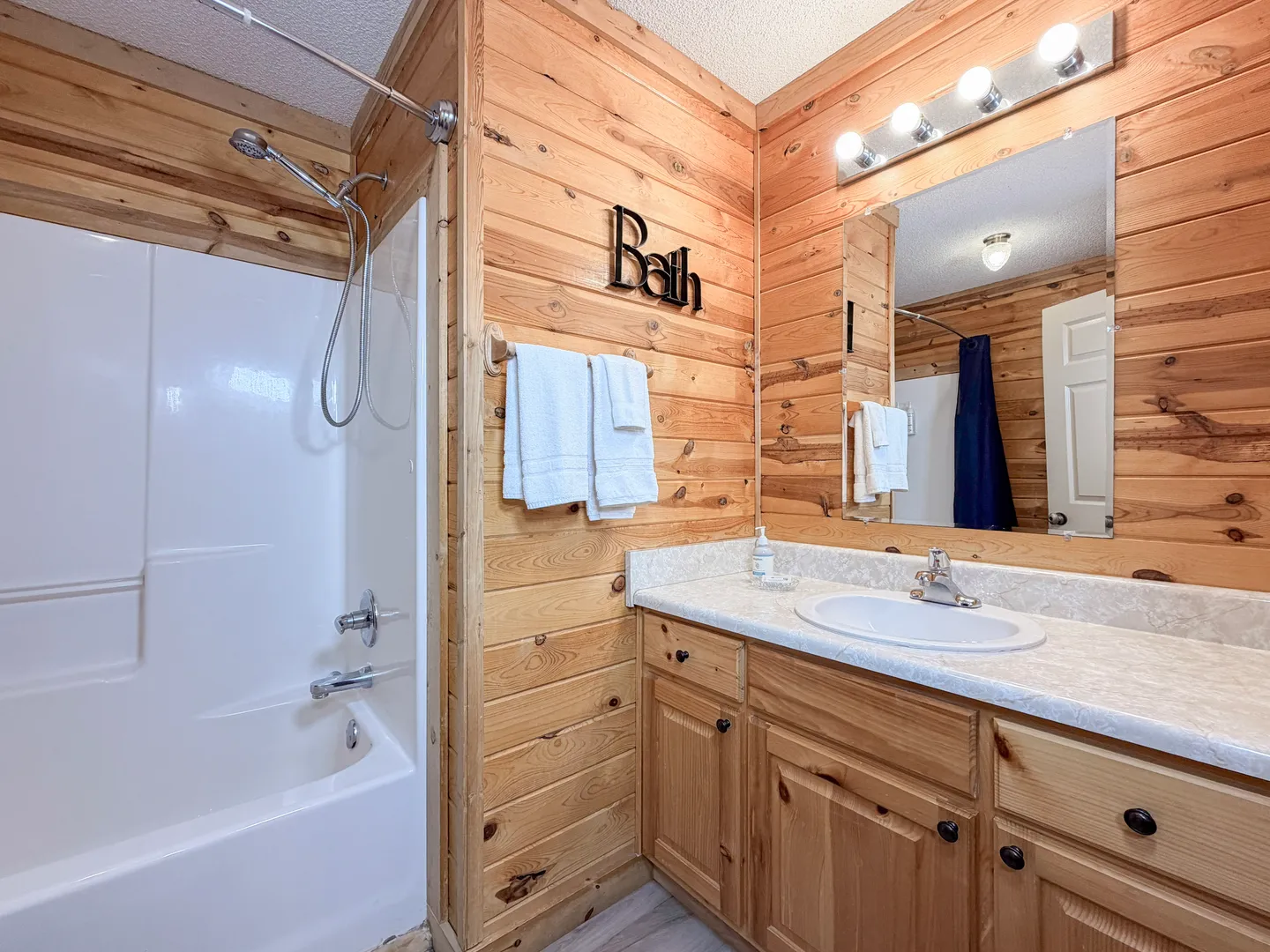 Bathroom with wood-paneled walls, vanity with mirror, and a white bathtub and shower surround.