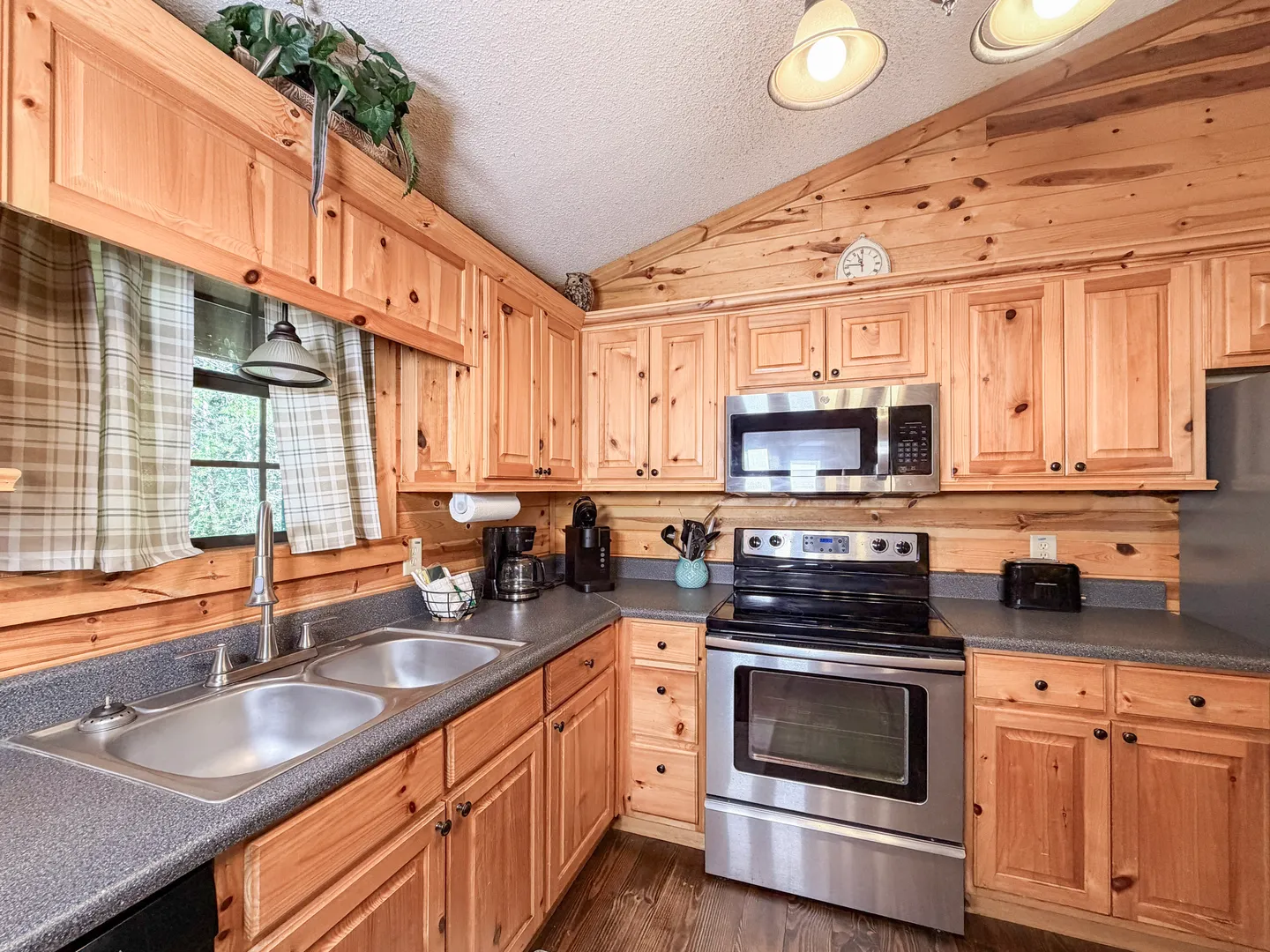 A kitchen with knotty pine cabinets and walls, speckled countertops, and stainless steel appliances.