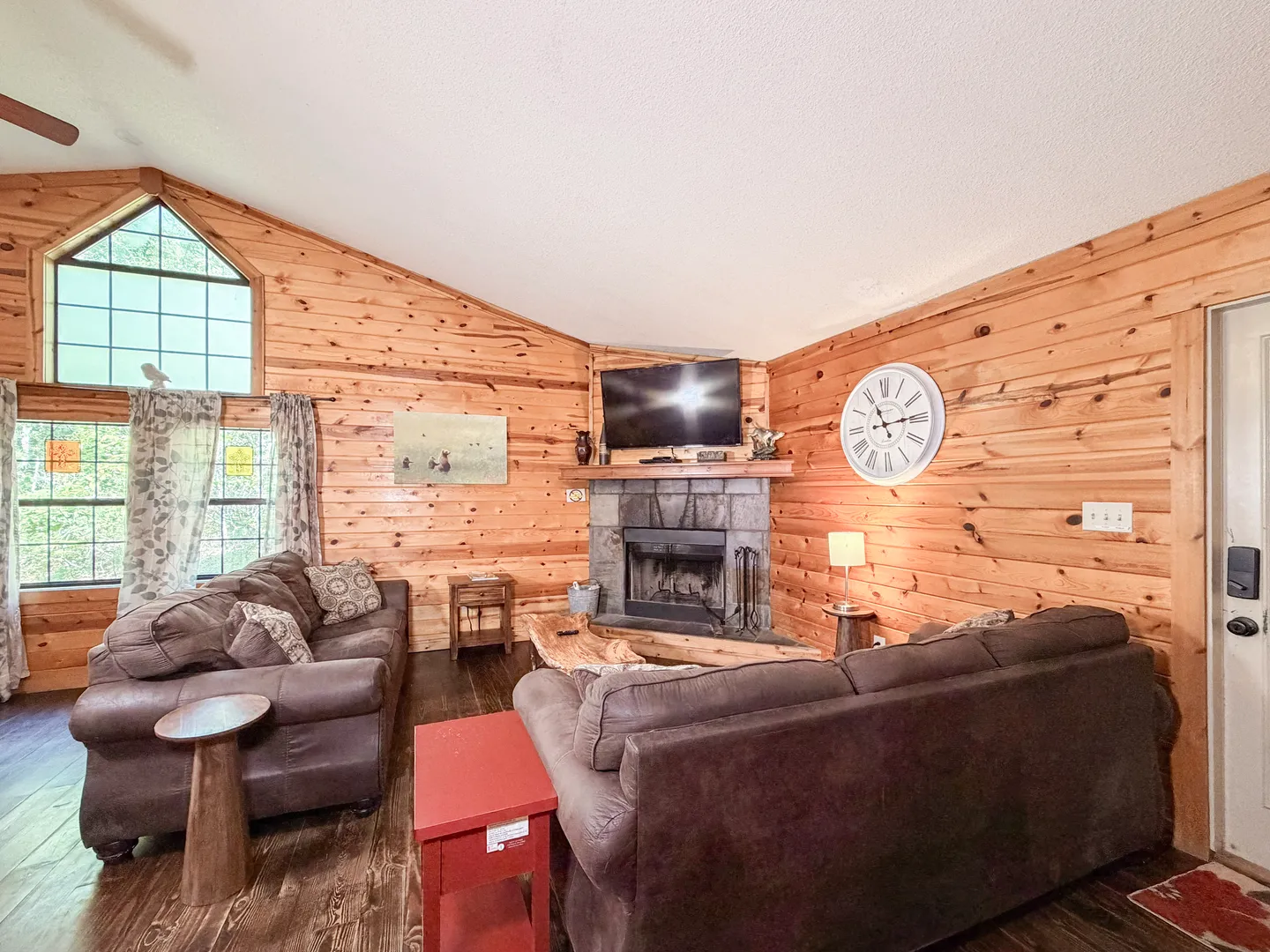 Living room with wood-paneled walls, stone fireplace with mounted television, and plush brown sofas.