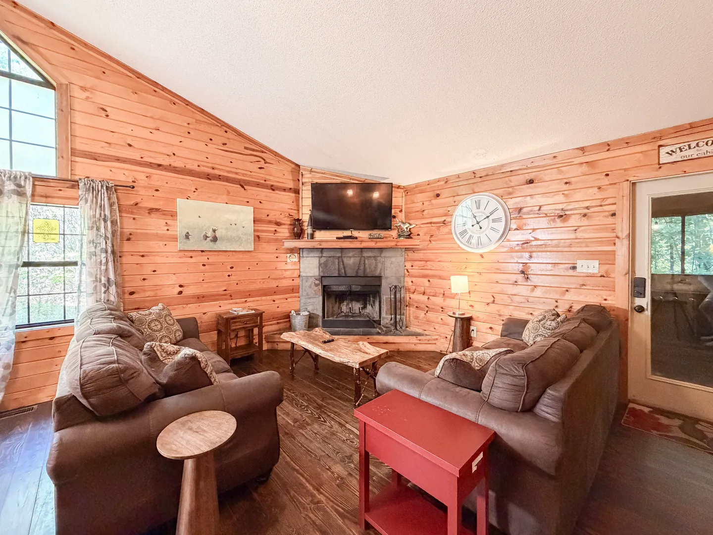 Living room with wood-paneled walls, two brown sofas, a stone corner fireplace, and a mounted television.