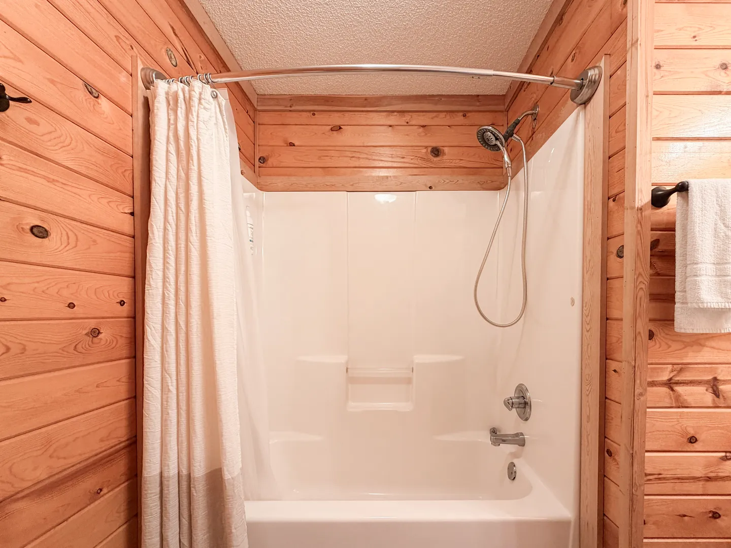 Bathroom with wood-paneled walls and a white bathtub and shower combination.