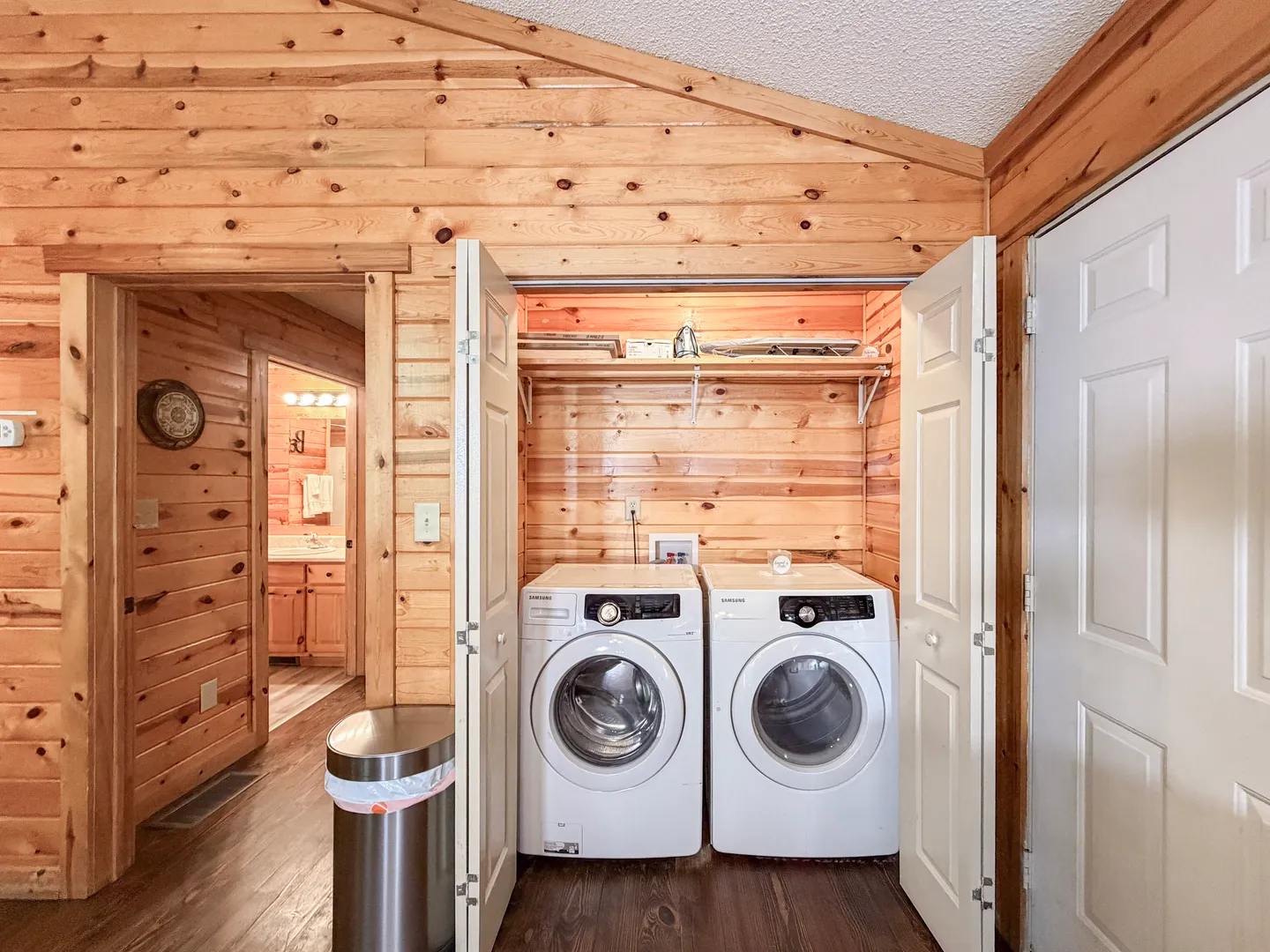 A laundry closet with double doors open to reveal a front-loading washer and dryer against wood-paneled walls.