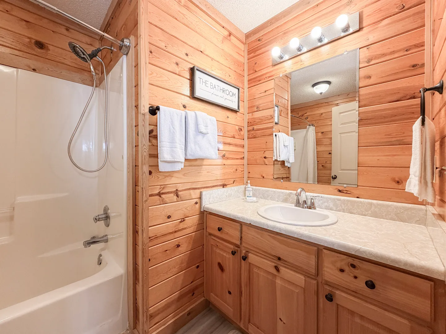 Bathroom with wood-paneled walls, a vanity with a white countertop and wood cabinets, and a white shower and bathtub combination.
