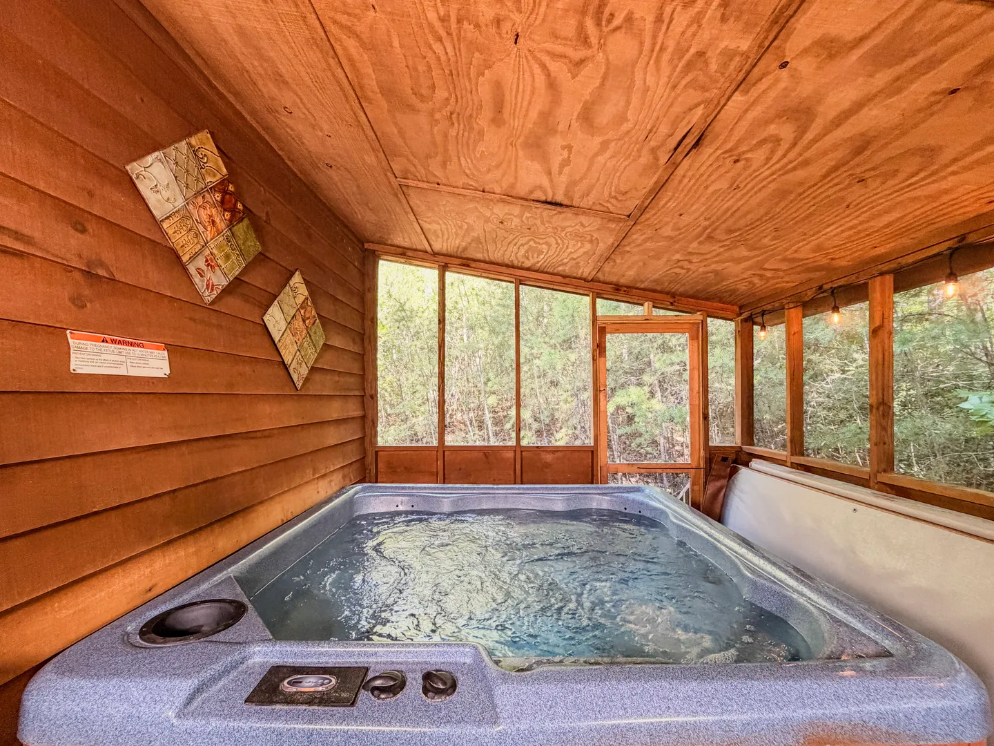 A hot tub with running water inside a wood-paneled screened-in porch with views of the surrounding trees.