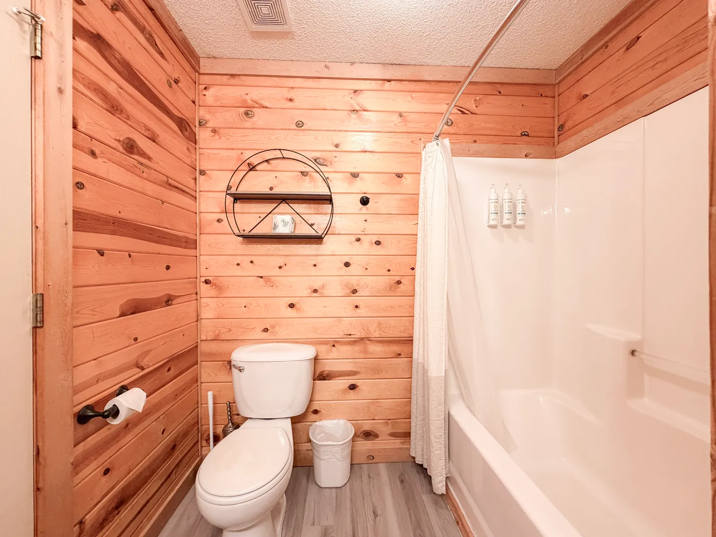 Bathroom with wood-paneled walls, a white toilet, and a white bathtub-shower combo.