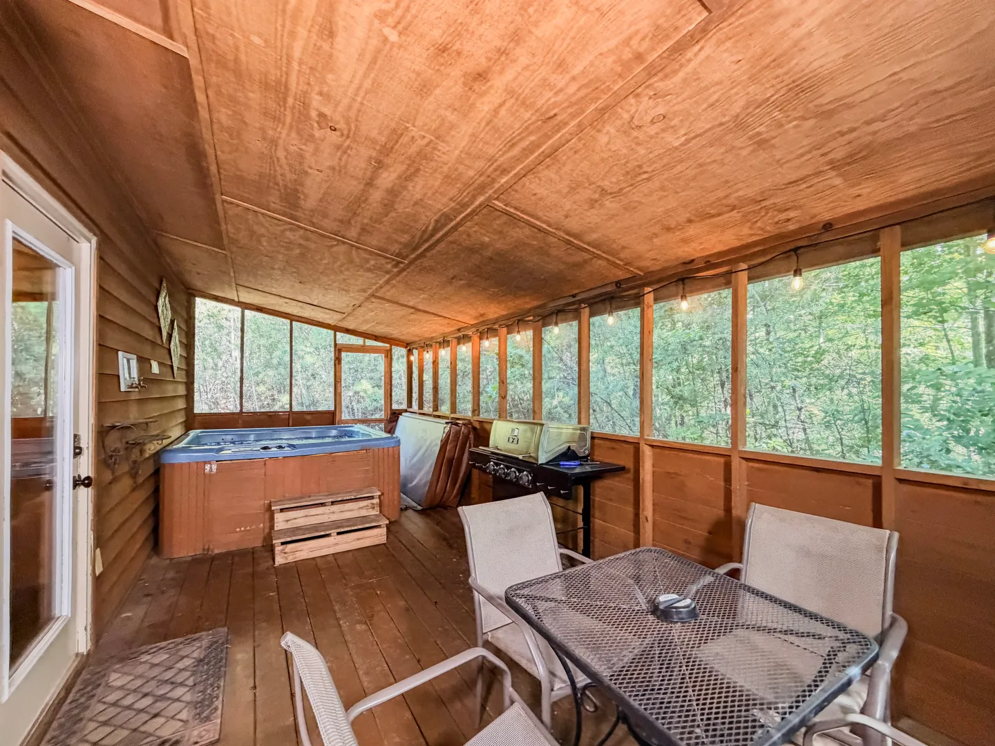 Screened-in porch featuring a hot tub, barbecue grill, and outdoor table and chairs.