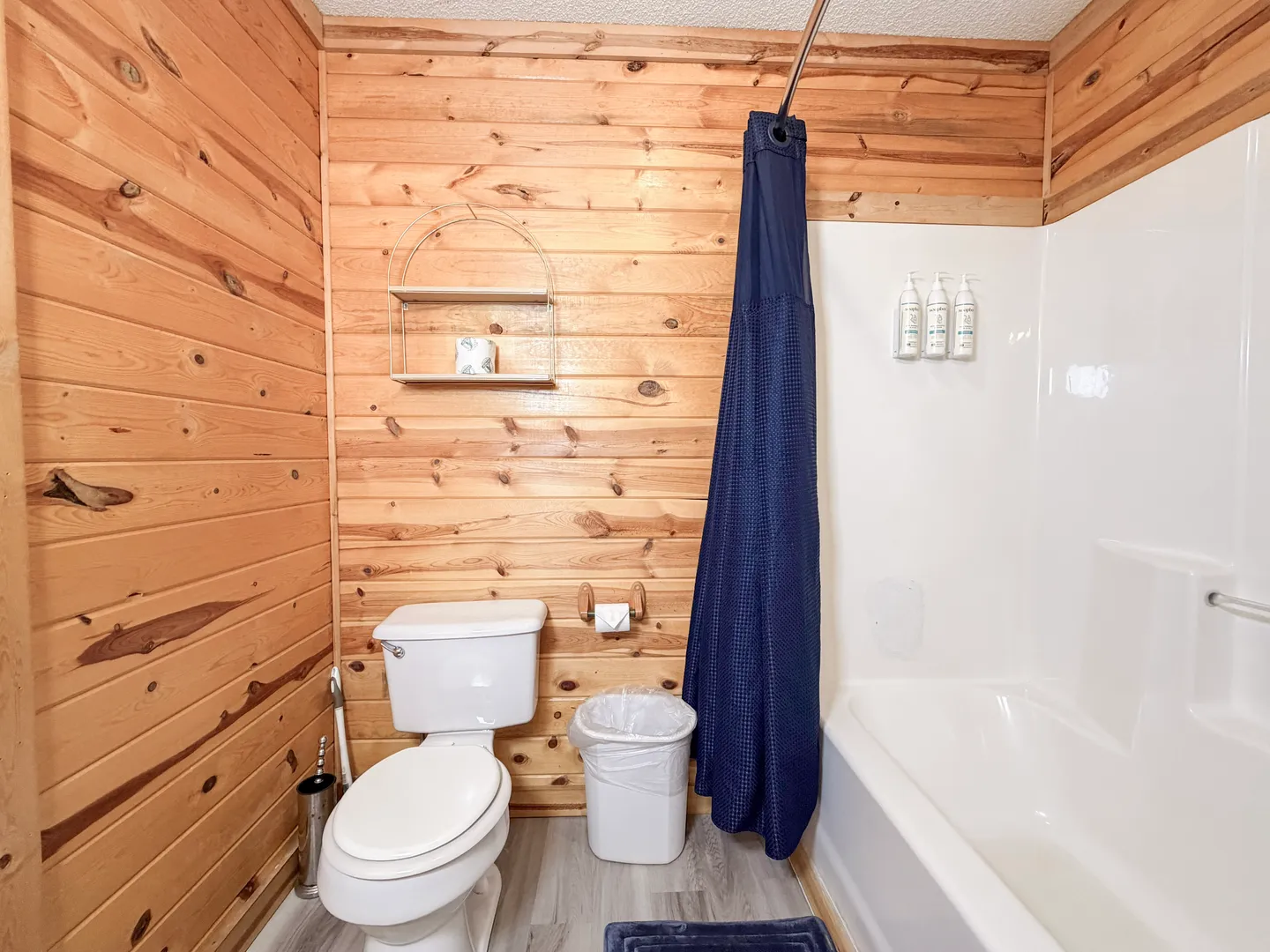 Bathroom with wood-paneled walls, a white toilet, and a white bathtub-shower combo with a navy blue curtain.
