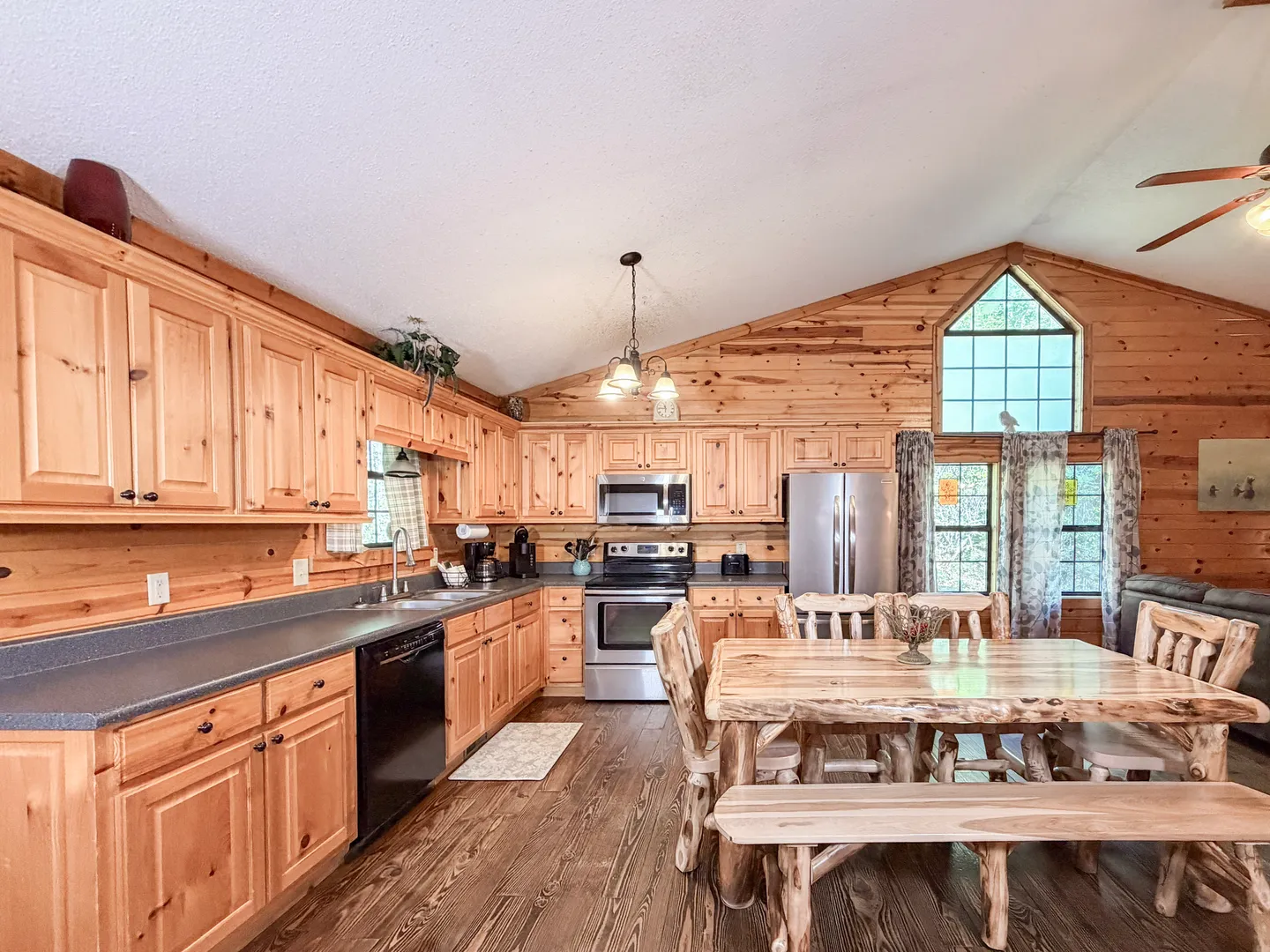 Open-concept cabin kitchen with pine cabinetry, stainless steel appliances, and a rustic wooden dining table with bench seating.