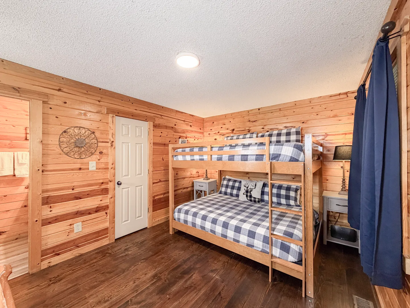 Bedroom with log-paneled walls, dark wood flooring, and a wooden bunk bed with blue and white plaid bedding.